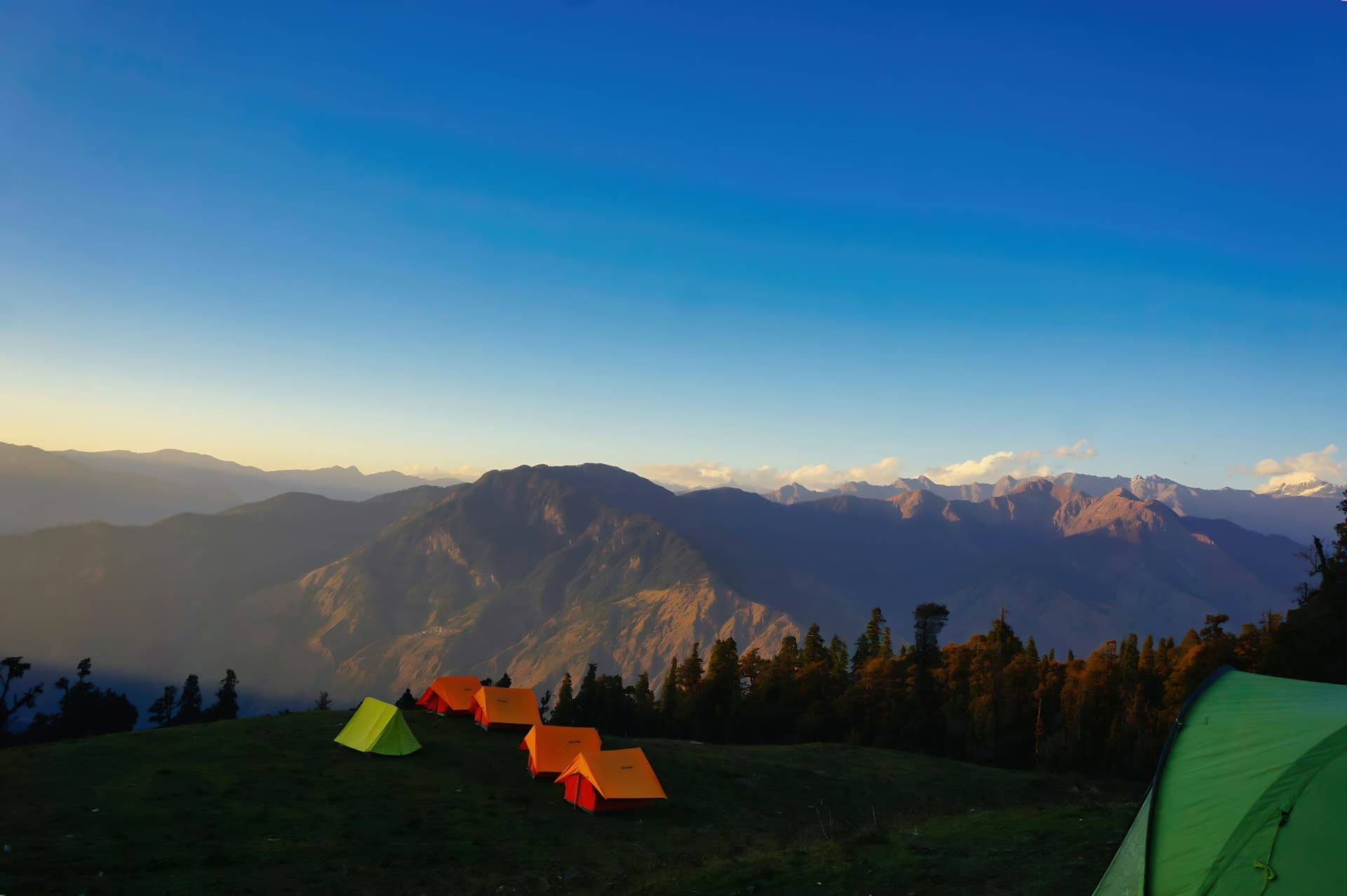 Orange tents on a high meadow at dusk, with mountain ranges fading into the distance